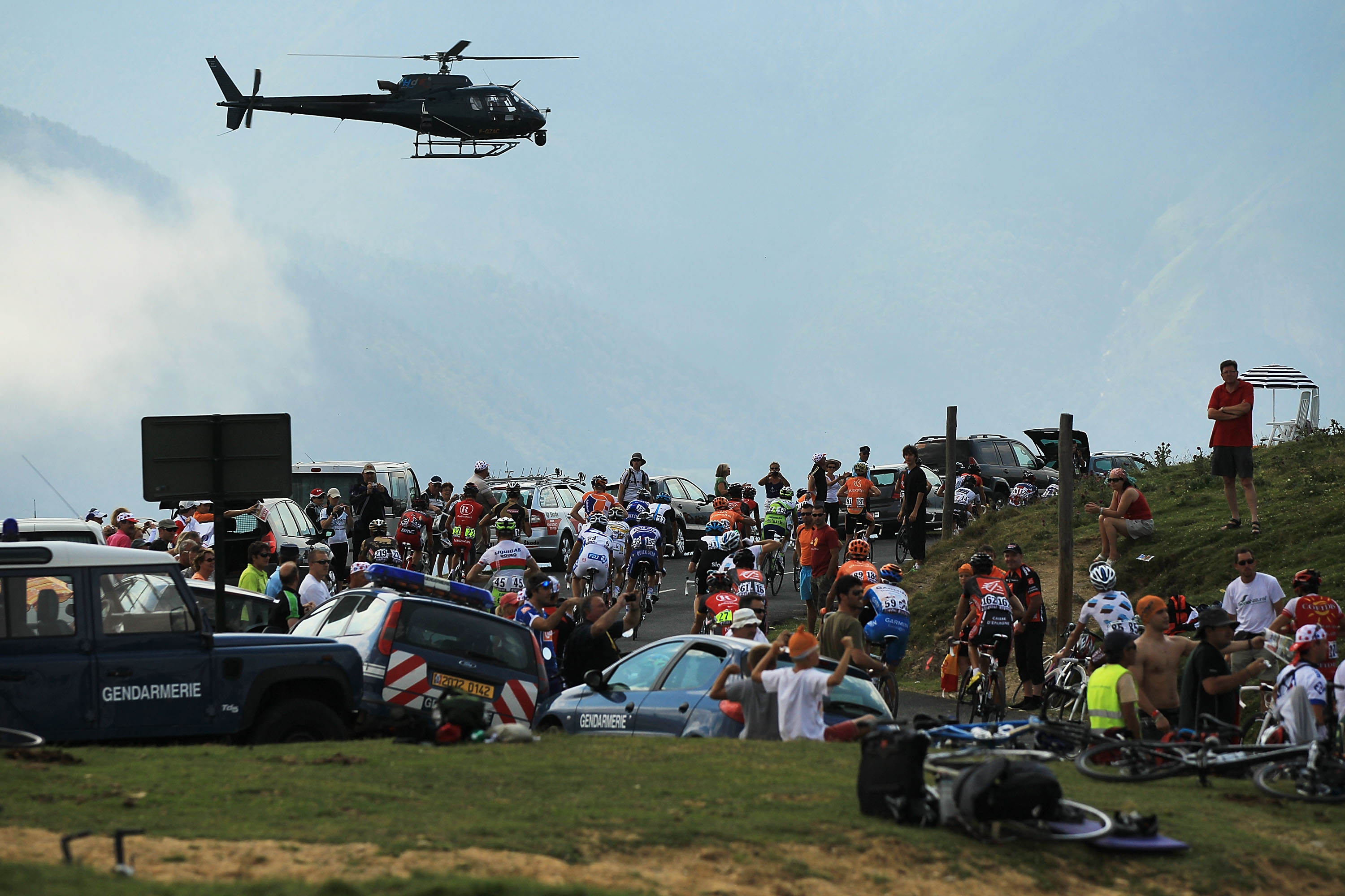 Peloton at the 2020 Tour de France with cars parked and helicopter above