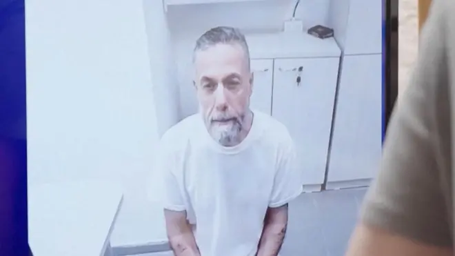 El médico palestino detenido, Hassam Abu Safiya, aparece en una pantalla vestido con una camisa blanca en prisión durante una audiencia ante la Corte Suprema israelí el 10 de junio de 2026.