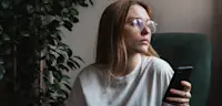 Sad upset girl holding smartphone looking out window at home, feeling frustrated receiving text message with bad news feeling lonely breaking up online chatting with boyfriend. Depressed woman scrolling social media